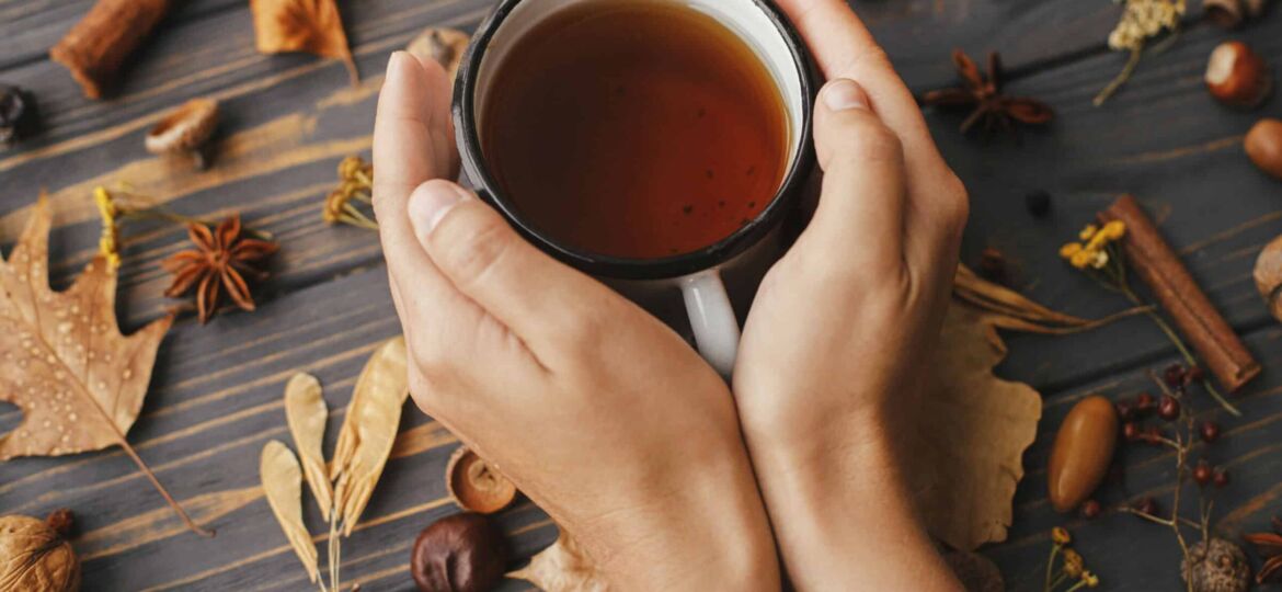 Hands holding warm cup of tea on background of autumn leaves, be