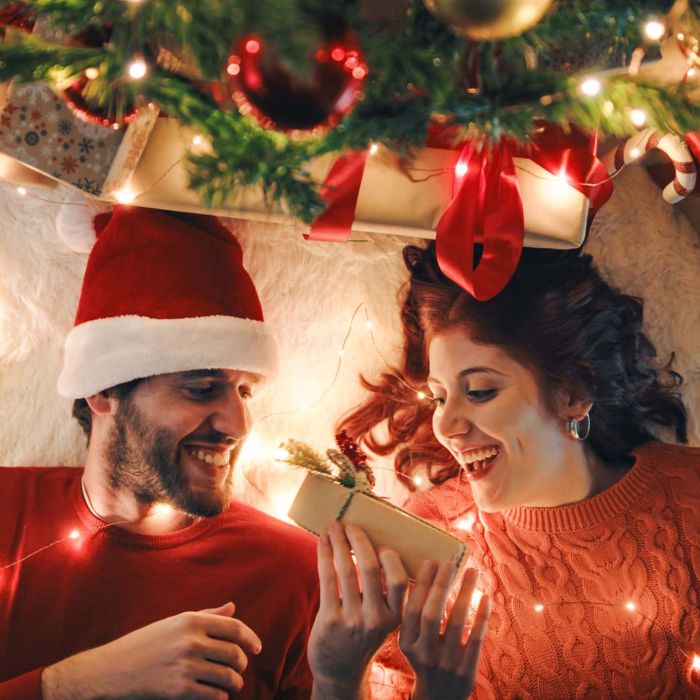 girl-gives-christmas-gift-to-boy-lying-under-tree-2023-11-27-05-11-15-utc