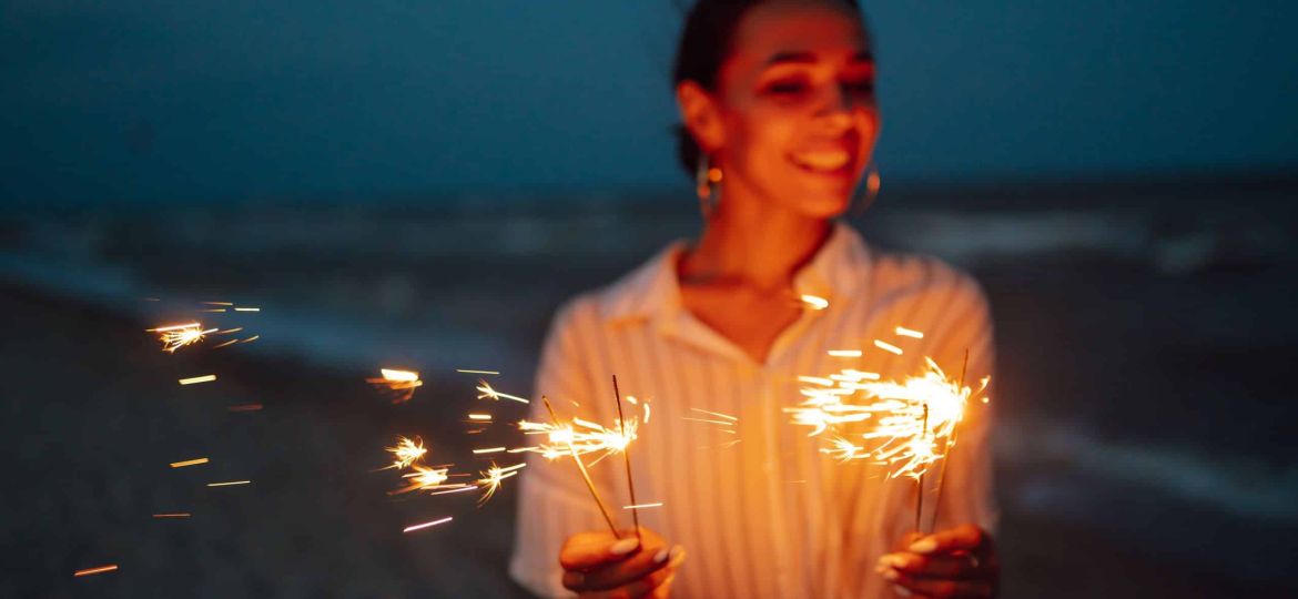 Glowing sparkles in hands. Women with Christmas sparklers on nature and twillight sky background.