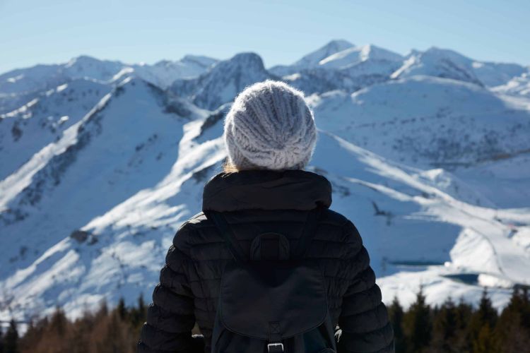 Woman with wool hat looking at mountains with snow in a sunny wi