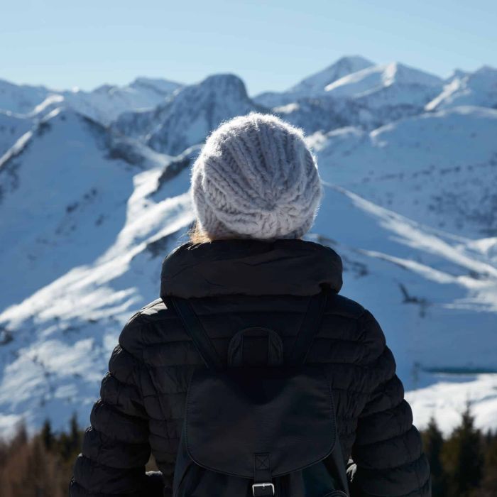 Woman with wool hat looking at mountains with snow in a sunny wi